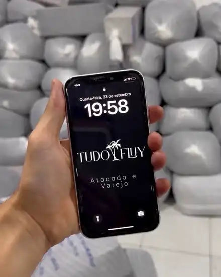 Celular com a marca TUDO FLUY em frente ao estoque da fábrica