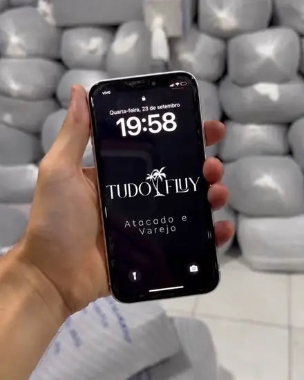 Celular com a logo TUDO FLUY Atacado e Varejo diante do estoque real da marca
